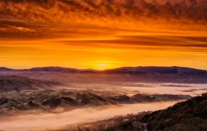 image_desktop 10 | Axxcess Platform Golden sunset over rolling hills with low-lying fog in a valley; warm orange sky above silhouetted ridges.
