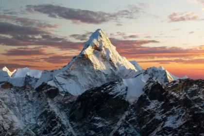 Snowy, jagged mountain peak bathed in golden sunset light with a colorful sky