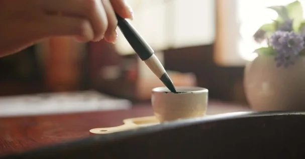 fjklds | Axxcess Platform Person using a brush to glaze a small ceramic cup on a wooden table with a blurred background.