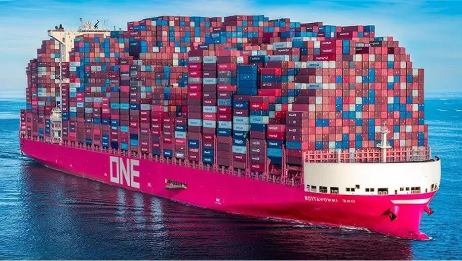Large pink cargo ship named ONE sails on calm blue sea, fully loaded with multicolored shipping containers.