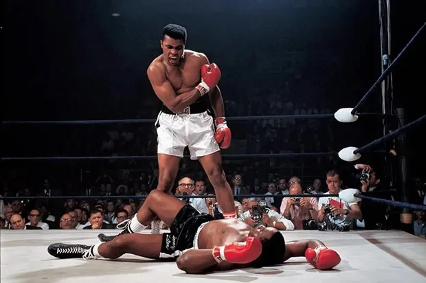image_desktop 22 | Axxcess Platform Boxer in white trunks stands over a fallen opponent with red gloves inside a boxing ring as spectators watch from the crowd.